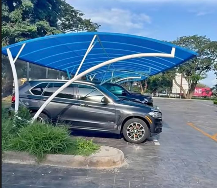 Two curved blue polycarbonate carports on white cantilever arms, covering an SUV on a paved forecourt